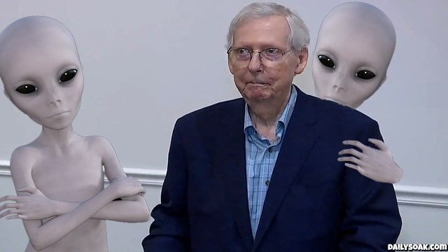 Mitch McConnell freezing during a speech while surrounded by gray aliens.