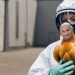 WHO worker wearing hazmat suit holding a chicken with the head of Dr. Fauci.