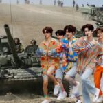 South Korean K-Pop boy band dancing in colorful outfits in front of Russian soldiers in Ukraine.