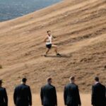 Secret Service agents watching man run up a sloped ground hill.