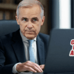 Canada Prime Minister Mark Carney sitting at desk looking at laptop.