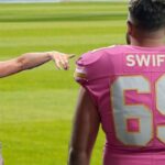 Travis Kelsey wearing a football jersey as Taylor Swift points and laughs at him.