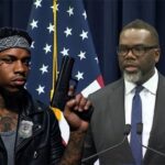 Black Chicago Mayor Brandon Johnson on stage next to a male, black gang member.