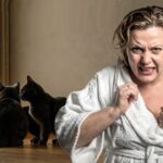 Crazy, liberal white woman standing in a room with numerous black cats.