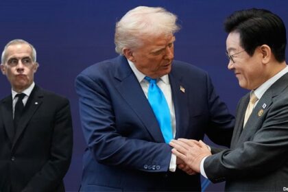 Mark Carney standing in a corner watching President Donald Trump during APEC summit in South Korea.