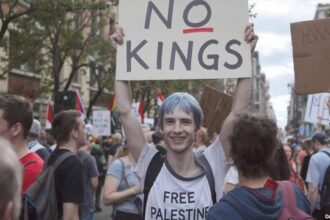 Blue-haired, skinny white man holding up a "No Kings" sign.