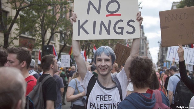Blue-haired, skinny white man holding up a "No Kings" sign.