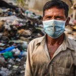 Indian man wearing face mask surrounded by trash and poop in dirty India street.