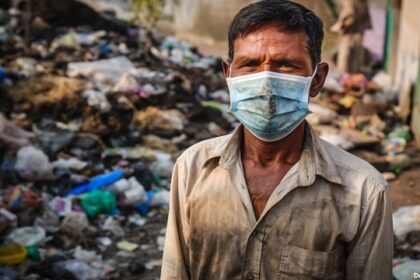 Indian man wearing face mask surrounded by trash and poop in dirty India street.