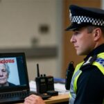 UK police man sitting at a laptop looking at an old British woman on the screen.