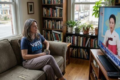 Female CNN viewer sitting on a couch watching North Korean news on television.