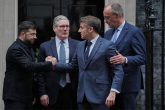European leaders UK Prime Minister Keir Starmer, Volodymyr Zelensky, Friedrich Merz, and Emmanuel Macron hugging on street in London.