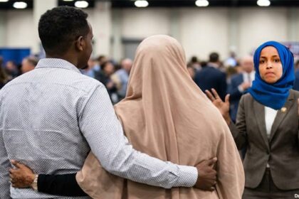 Ilhan Omar wearing Muslim hijab staring angrily at her brother holding another Somali woman.