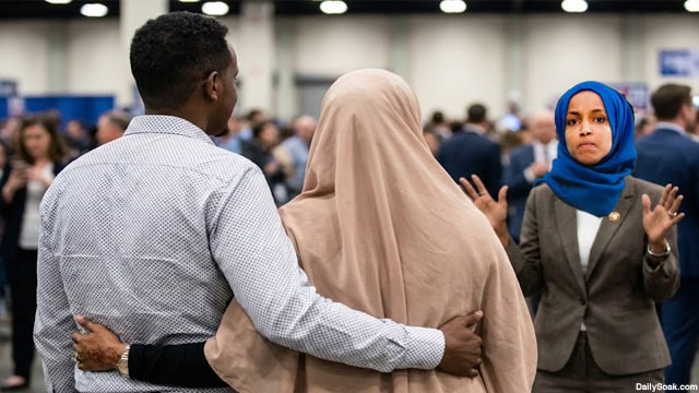 Ilhan Omar wearing Muslim hijab staring angrily at her brother holding another Somali woman.