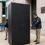 DOJ agents in front of the redacted Jeffrey Epstein files full of black rectangles.