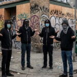 Masked anti-ICE rioters standing in front of a trashy, downtrodden Los Angeles, California street.