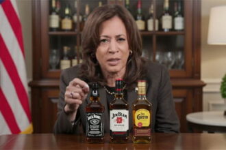 Kamala Harris speaking at a table lined with alcoholic bottles.
