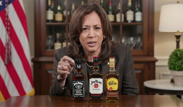 Kamala Harris speaking at a table lined with alcoholic bottles.