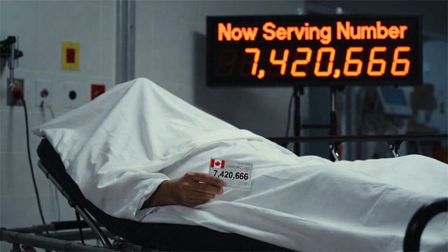 Canadian man lying on a gurney under a white sheet inside of a Canada hospital emergency room.