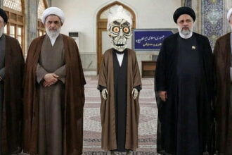 Achmed the Dead Terrorist wearing Iranian clothing standing next to Iran leadership inside of a room.