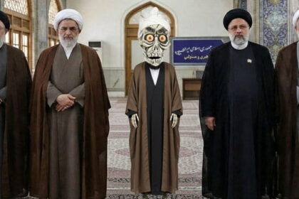 Achmed the Dead Terrorist wearing Iranian clothing standing next to Iran leadership inside of a room.