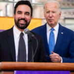 Mayor Mamdani standing next to Joe Biden behind a podium both wearing suits.