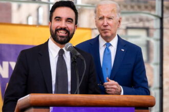 Mayor Mamdani standing next to Joe Biden behind a podium both wearing suits.