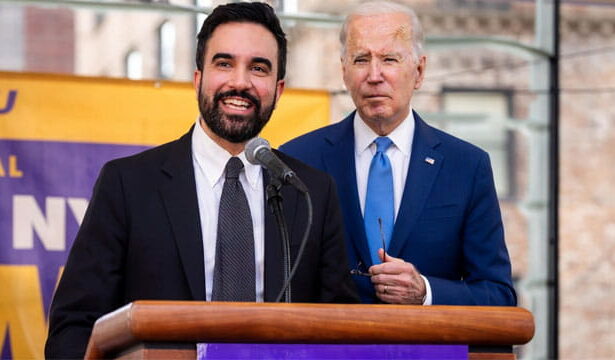 Mayor Mamdani standing next to Joe Biden behind a podium both wearing suits.