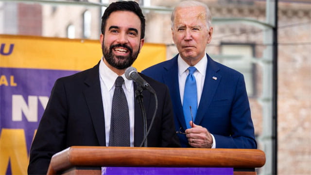 Mayor Mamdani standing next to Joe Biden behind a podium both wearing suits.