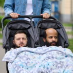 Woman pushing a baby stroller with Zelensky and a Somali man in it in front if an IRS tax building.