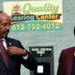 Ilhan Omar wearing Islamic clothing standing next to Somali man in front of Quality Learing Center.