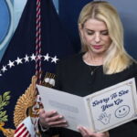 Blonde female Pam Bondi reading a letter on stage at the White House press room.