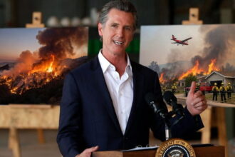 California Governor Gavin Newsom speaking at a podium in front of images of wildfires.