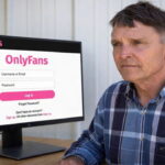 Ed Gallrein sitting at a desk looking at a computer screen on the OnlyFans website.