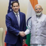 Marco Rubio shaking hands with Indian Prime Minister Modi on stage in front of flags.