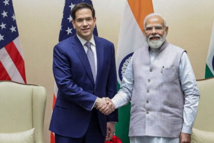 Marco Rubio shaking hands with Indian Prime Minister Modi on stage in front of flags.