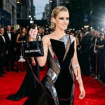 Met Gala celebrity holding a Balenciaga bag with a red Adrenochrome IV in her arm.