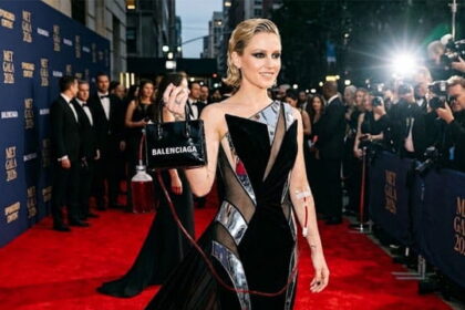 Met Gala celebrity holding a Balenciaga bag with a red Adrenochrome IV in her arm.