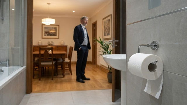 Thomas Massie standing in a dining room from the view from a bathroom showing a toilet and toilet paper.