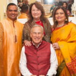 Texas Governor Greg Abbott wearing traditional Indian clothing sitting beside various male and female Indian H1B workers.