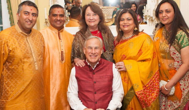 Texas Governor Greg Abbott wearing traditional Indian clothing sitting beside various male and female Indian H1B workers.