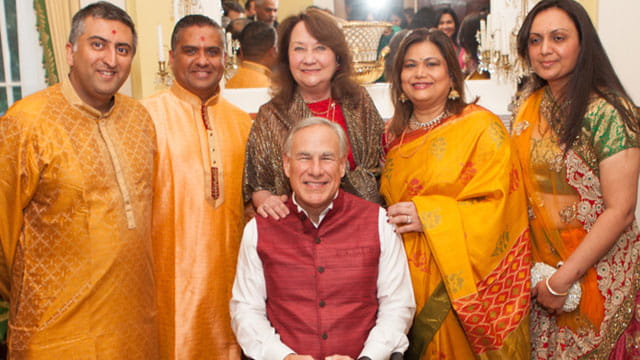 Texas Governor Greg Abbott wearing traditional Indian clothing sitting beside various male and female Indian H1B workers.