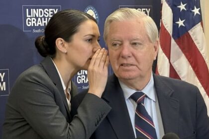 A female aide whispering into South Carolina Senator Lindsey Graham's ear on stage.