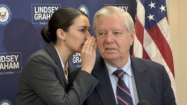 A female aide whispering into South Carolina Senator Lindsey Graham's ear on stage.