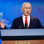 Israel Prime Minister Benjamin Netanyahu wearing a suit on stage speaking.