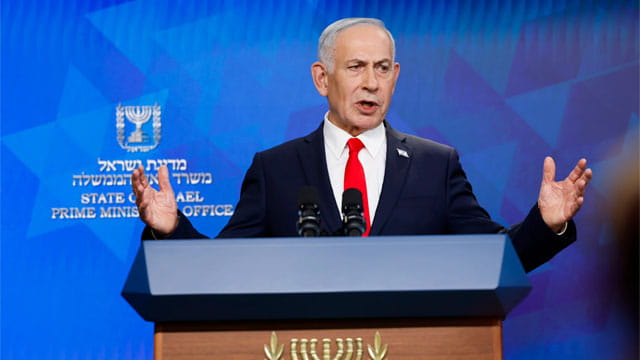 Israel Prime Minister Benjamin Netanyahu wearing a suit on stage speaking.