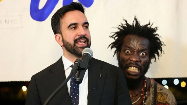 NYC Mayor Zohran Mamdani giving a speech on stage in front of a Haitian migrant.