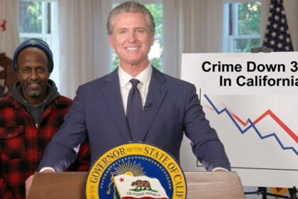 California Governor Gavin Newsom wearing a suit standing behind a podium and a male black Somali man on stage.