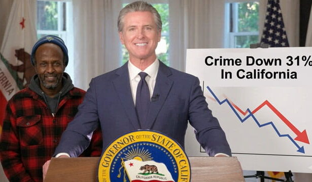California Governor Gavin Newsom wearing a suit standing behind a podium and a male black Somali man on stage.