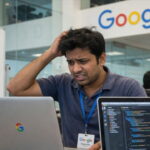 Male Indian H-1B worker sitting at a computer inside of Google office.